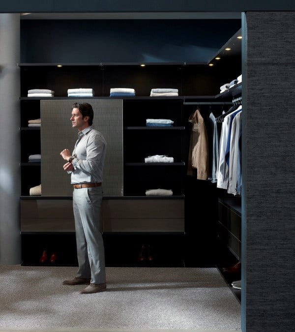 Man standing in a modern, organized walk-in closet with neatly arranged clothes and shelves