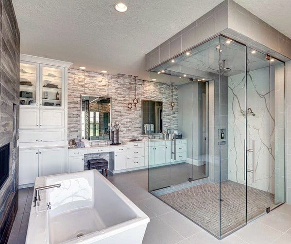 Luxury bathroom with glass shower, freestanding tub, stone accent wall, and dual vanities.