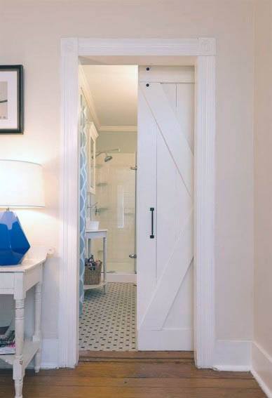 White barn-style pocket door with black hardware leads to a bright bathroom featuring patterned tile flooring and a glass shower