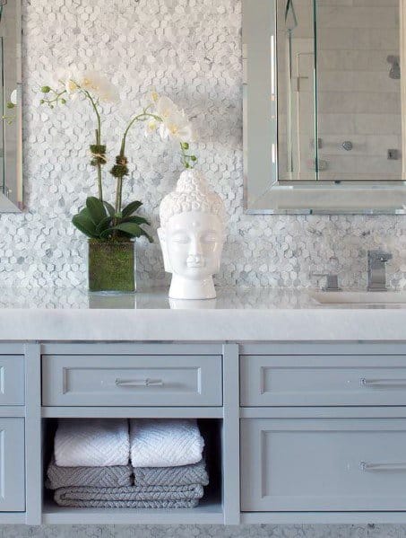 Bathroom with white pebble tile backsplash, light grey vanity, and decorative Buddha statue.