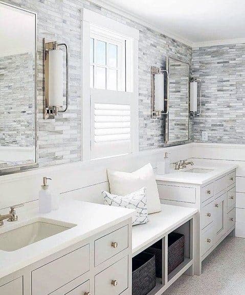 Elegant white bathroom with dual vanities, mosaic tile wall, and built-in bench seat.