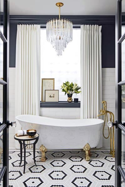 Elegant bathroom with a freestanding bathtub, gold fixtures, chandelier, and black-and-white hexagonal tile floor