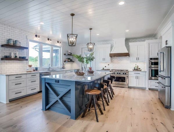 Spacious and stylish kitchen featuring light hardwood flooring, a modern blue island, white cabinetry, and a clean subway tile backsplash, offering a warm, traditional feel with a contemporary twist