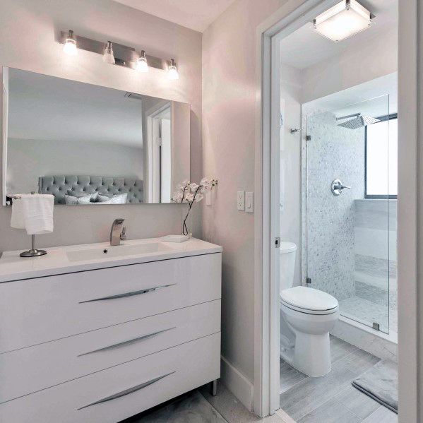 Modern bathroom with a sleek white vanity, large mirror, and white glass-enclosed shower