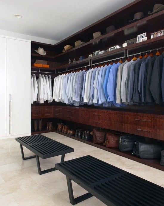 Spacious walk-in closet with neatly arranged clothes, hats, and bags, two black benches in the center