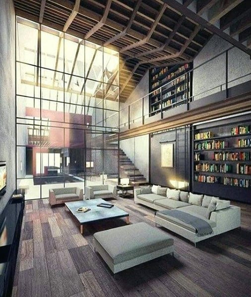 Spacious living room with high ceilings, large glass windows, modern furniture, and bookshelves.