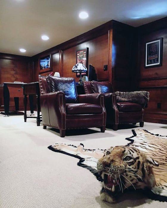 Luxurious mancave with wood-paneled walls, leather armchairs, tiger rug, and warm lighting.