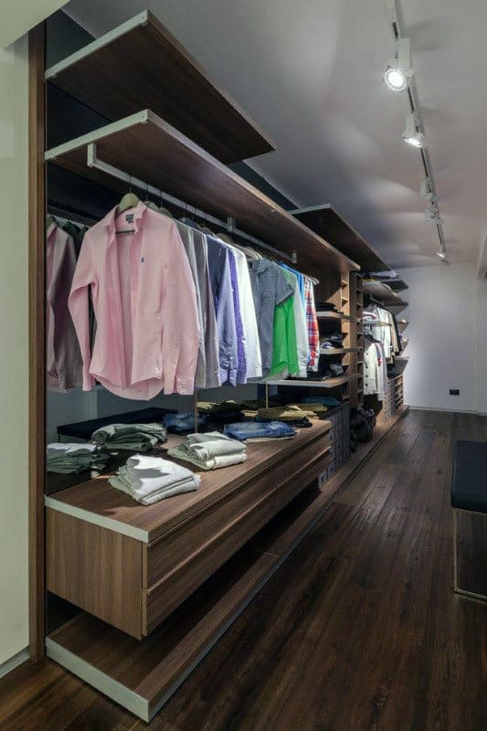 Walk-in closet with wooden shelves, hanging shirts, folded clothes, and track lighting on the ceiling