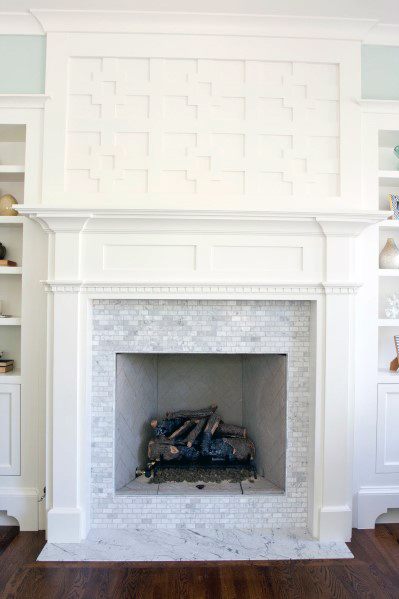 White fireplace with small marble mosaic tiles and decorative wood paneling above.