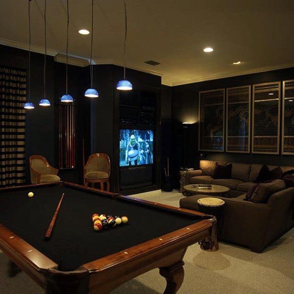 Cozy room with a pool table, plush seating, low-hanging lights, and a TV playing a movie