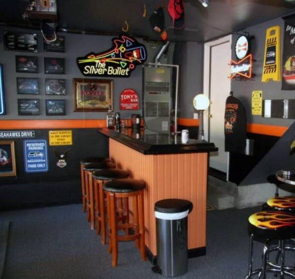 Garage bar with orange counter, wooden stools, neon signs, and sports-themed wall decor.