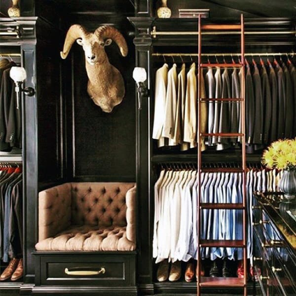 Luxurious closet with a ram head mounted, tailored suits, and a cozy seating area with a ladder to the right