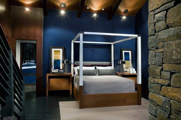 Modern navy bedroom with four-poster bed, stone accent wall, and wooden ceiling beams.