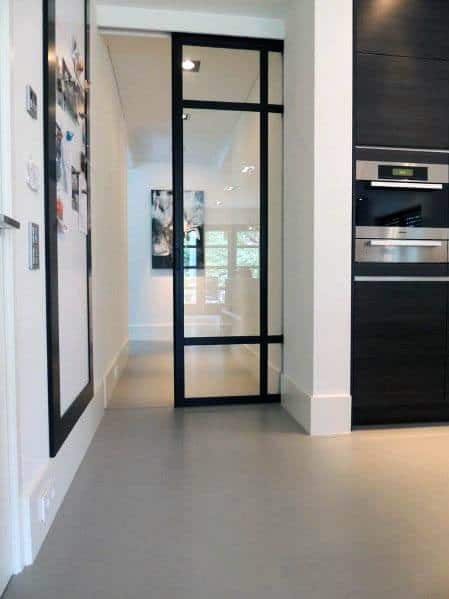 Modern black-framed glass pocket door opens to a bright hallway, featuring clean lines, minimalist design, and contemporary kitchen cabinetry