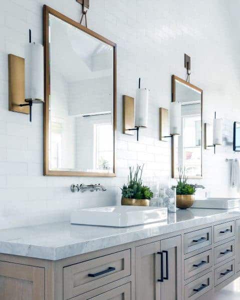 Double vanity bathroom with gold-framed mirrors, modern sconces, and potted greenery accents.