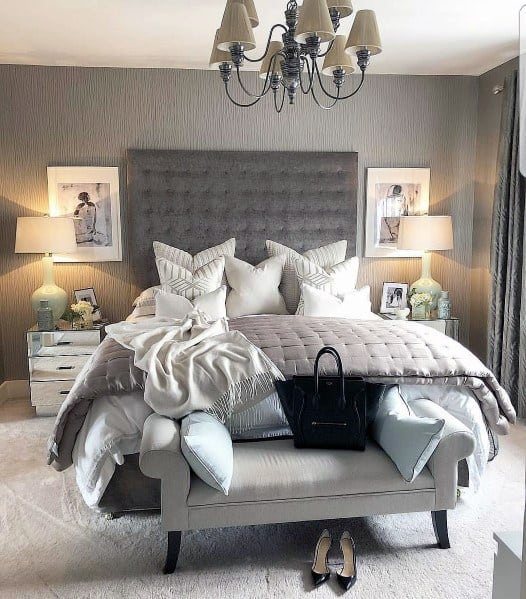 Elegant bedroom with tufted headboard, cozy bench, mirrored tables, and chandelier lighting.