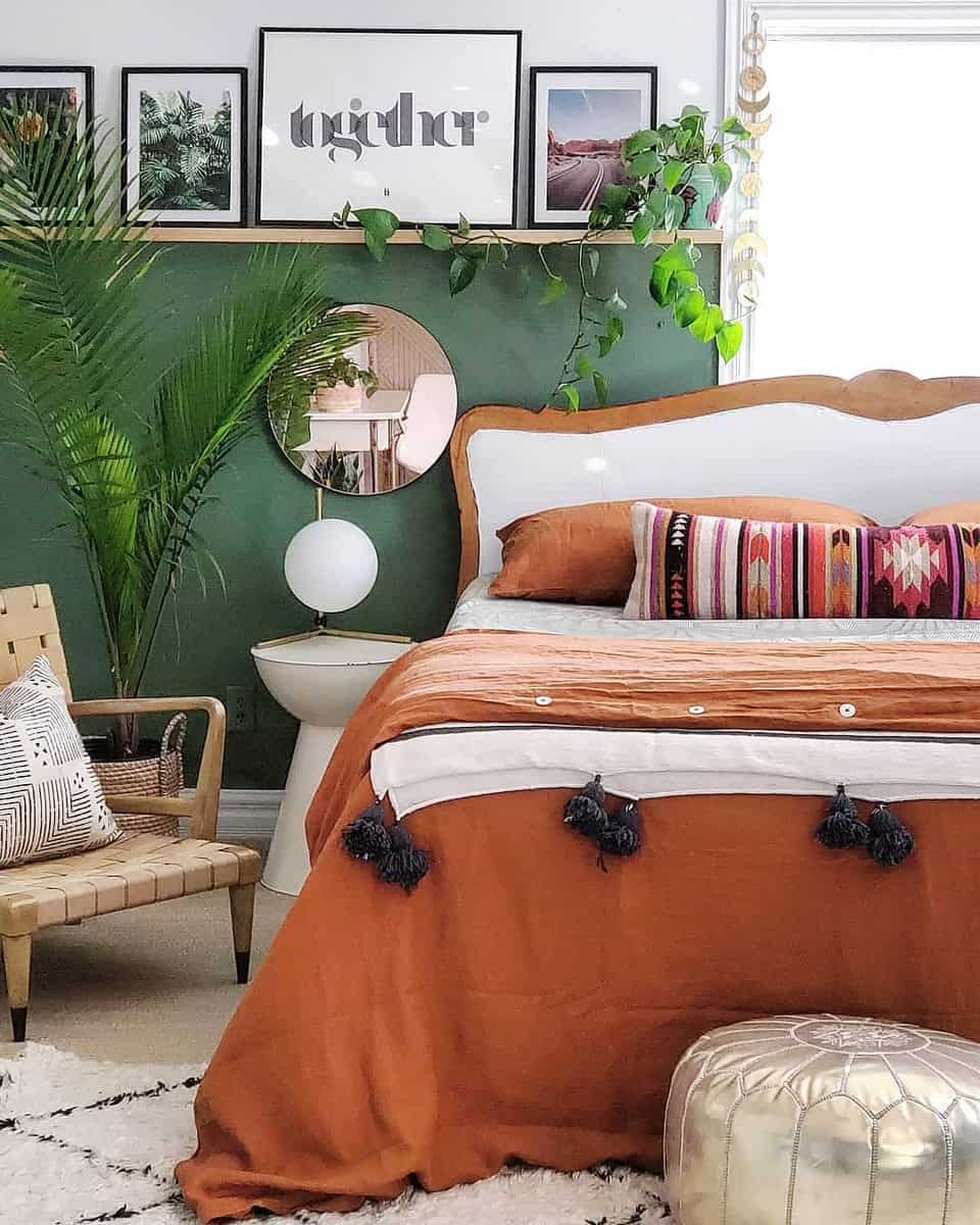 Cozy bedroom with green accent wall, wooden bed, orange bedding, patterned pillows, and leafy plants