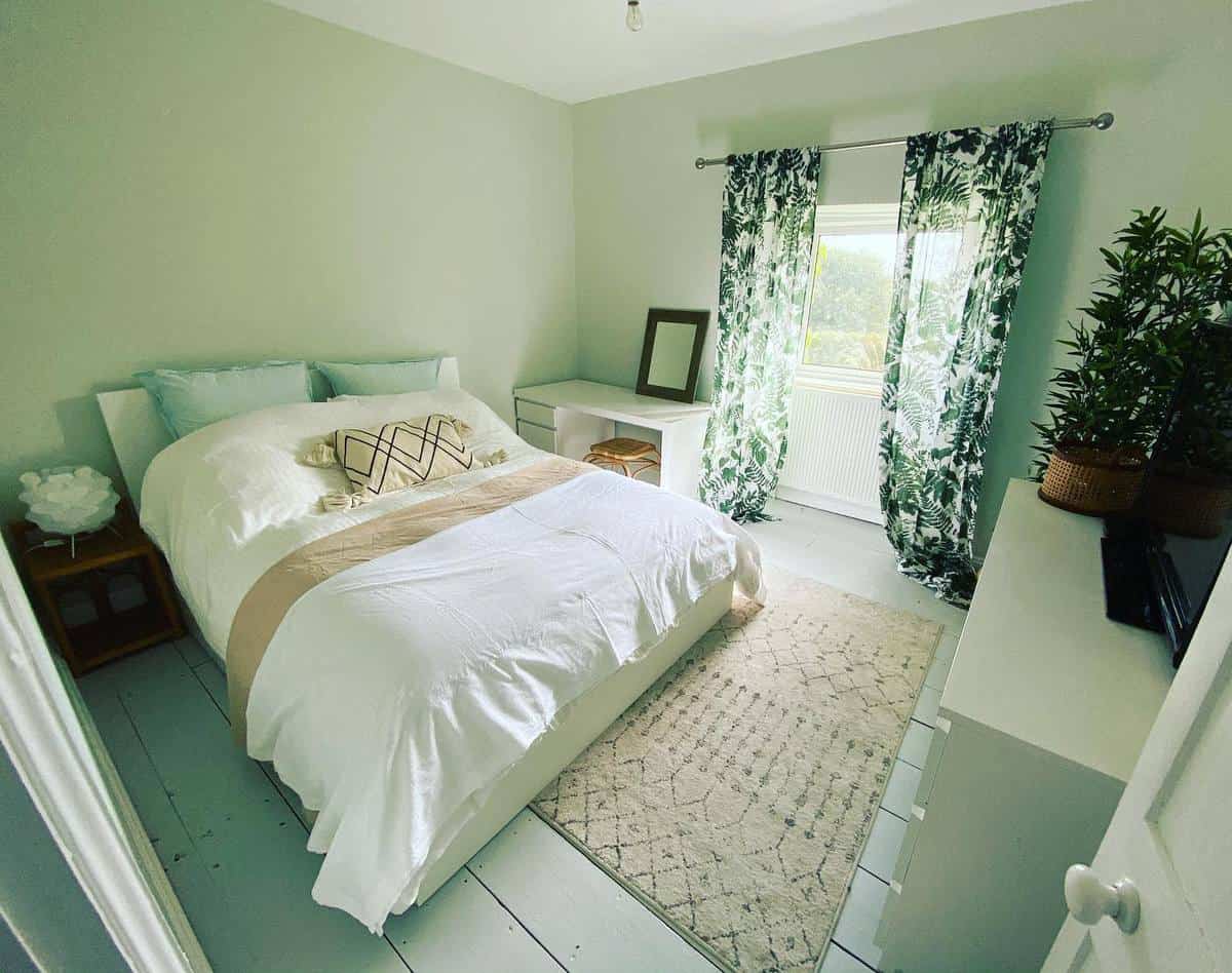 Cozy bedroom with a white bed, patterned curtains, a rug, and plants near a window