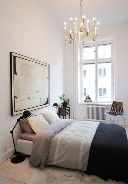 Scandinavian-style bedroom with minimal decor, large abstract art, and a gold chandelier.