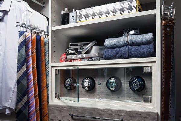 Closet shelf with watches in a display case, folded clothes, ties, shirts, and a travel-oriented book