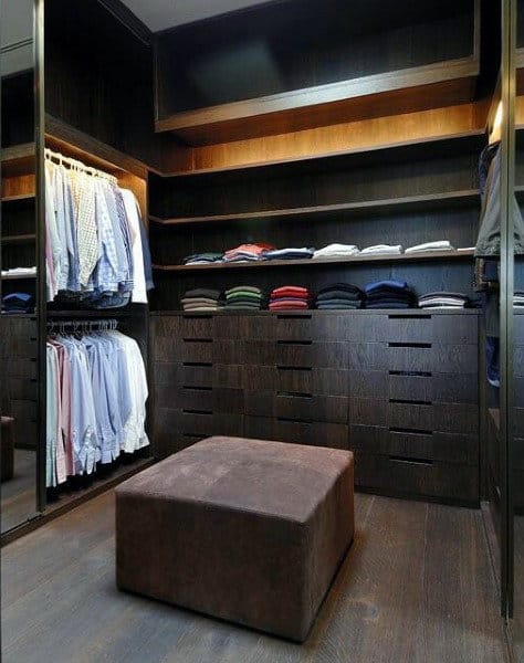 Modern walk-in closet with neatly arranged shirts, folded clothes, and a brown upholstered ottoman