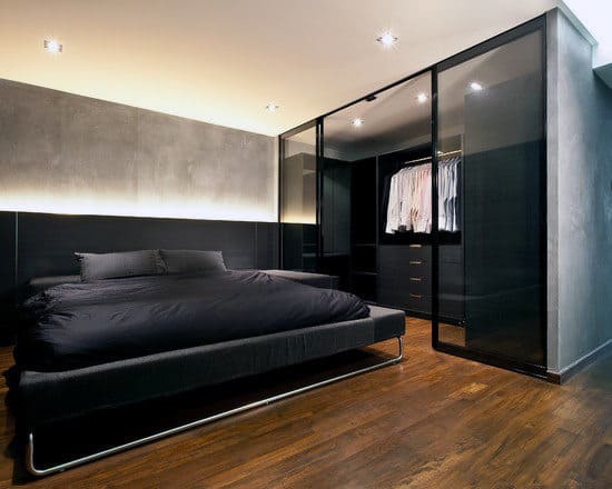 Minimalist bedroom with dark tones, featuring a sleek bed and a glass-door closet displaying shirts