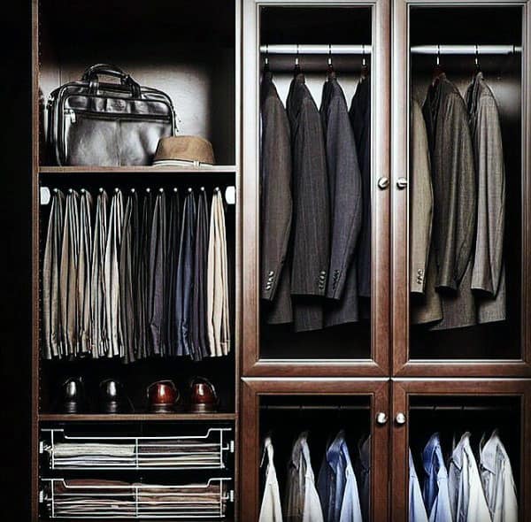 A neatly organized wooden wardrobe with suits, trousers, a bag, a hat, and shoes