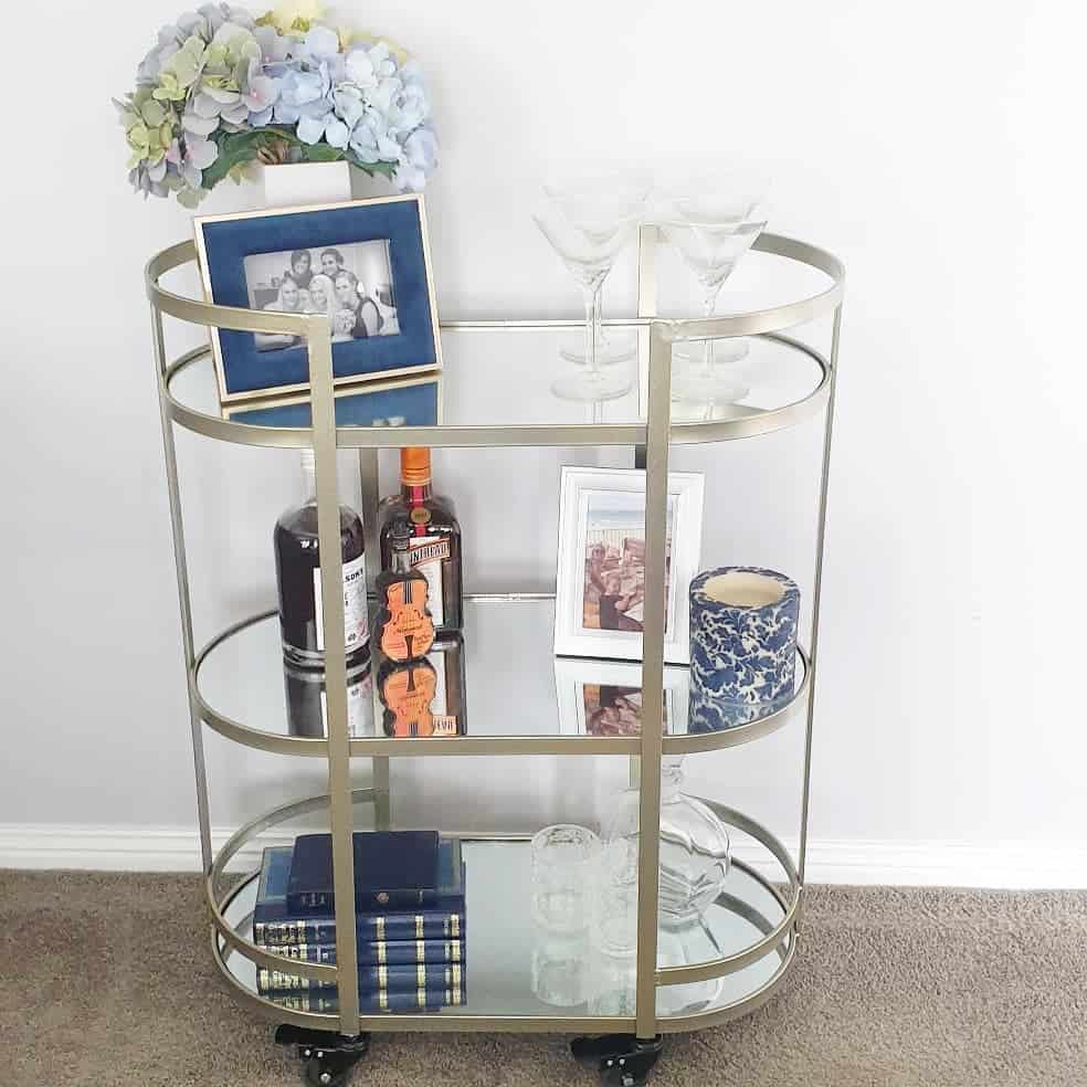 Metal bar cart with martini glasses, liquor bottles, framed photos, and decorative books.