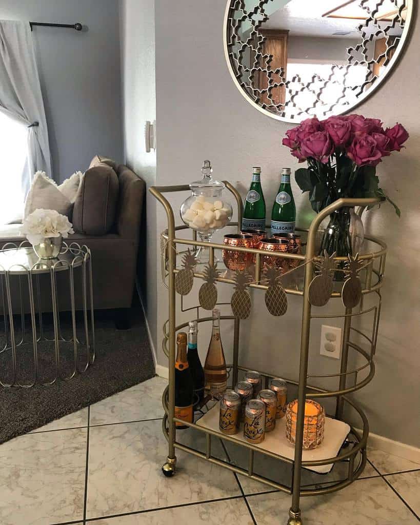 Gold-plated bar cart with pineapple accents, copper mugs, roses, and sparkling water bottles.