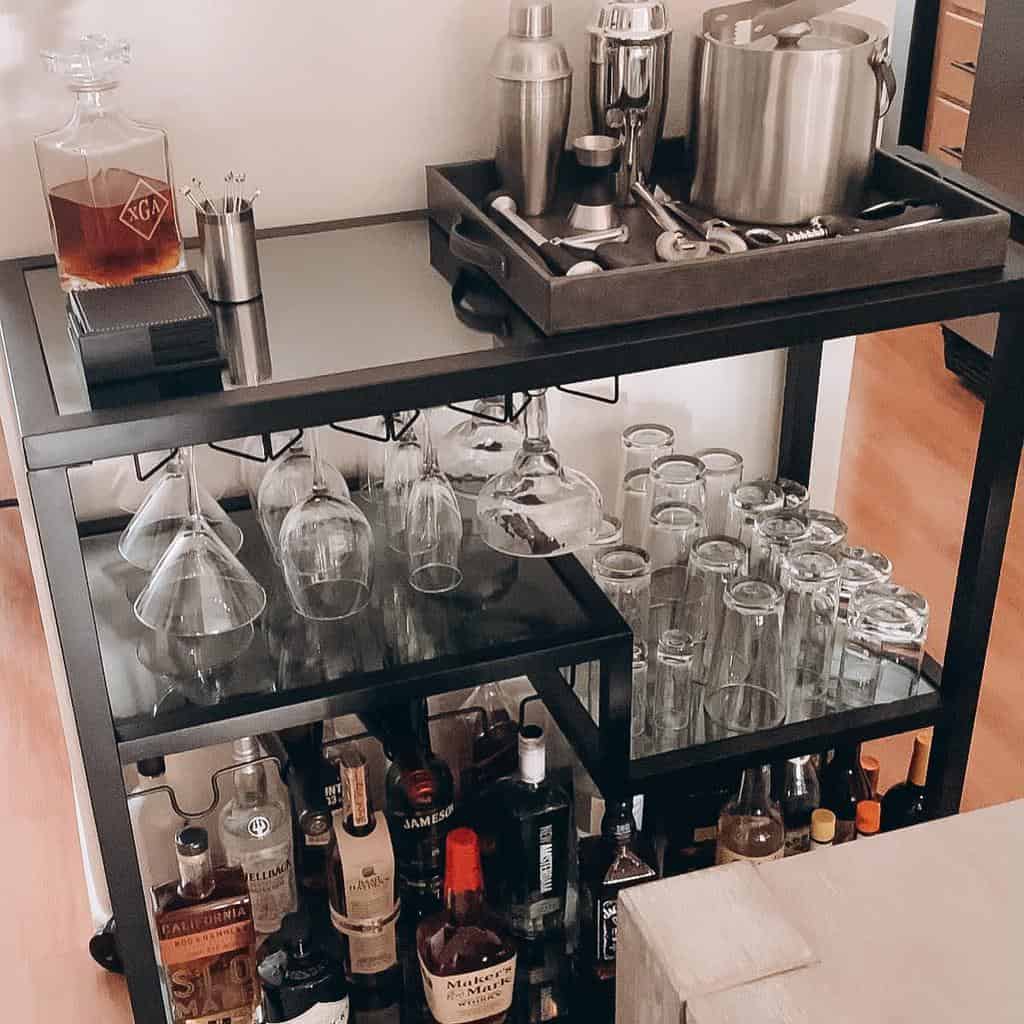 Black metal bar cart with liquor bottles, glassware, and cocktail tools.