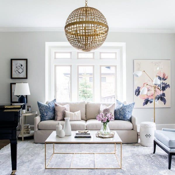 Modern living room with beige sofa, gold accents, large window, and decorative chandelier.