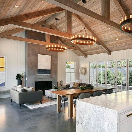 Spacious living room with vaulted wood ceiling, modern furniture, large windows, and circular chandeliers