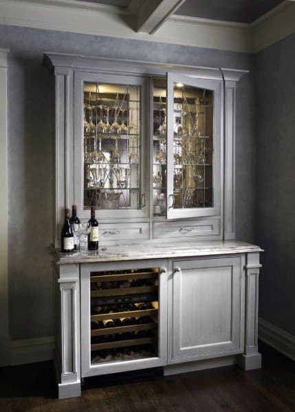 Classic home mini bar with white cabinetry, glass-paneled display doors, a built-in wine cooler, and marble countertop.