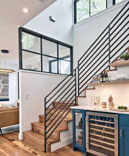 Stylish under-stair mini bar with blue cabinets, wine fridge, wood shelves, and modern railing design.