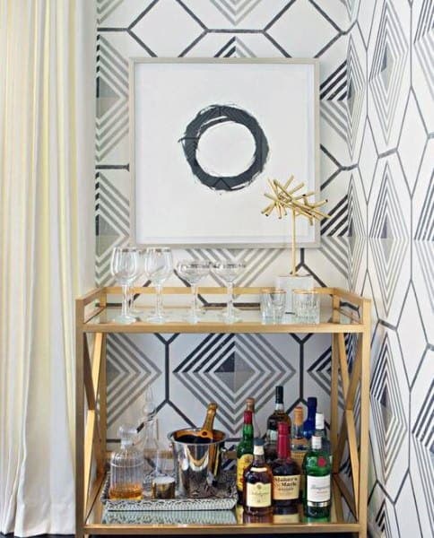 Gold bar cart with geometric wallpaper, bottles, and glassware.