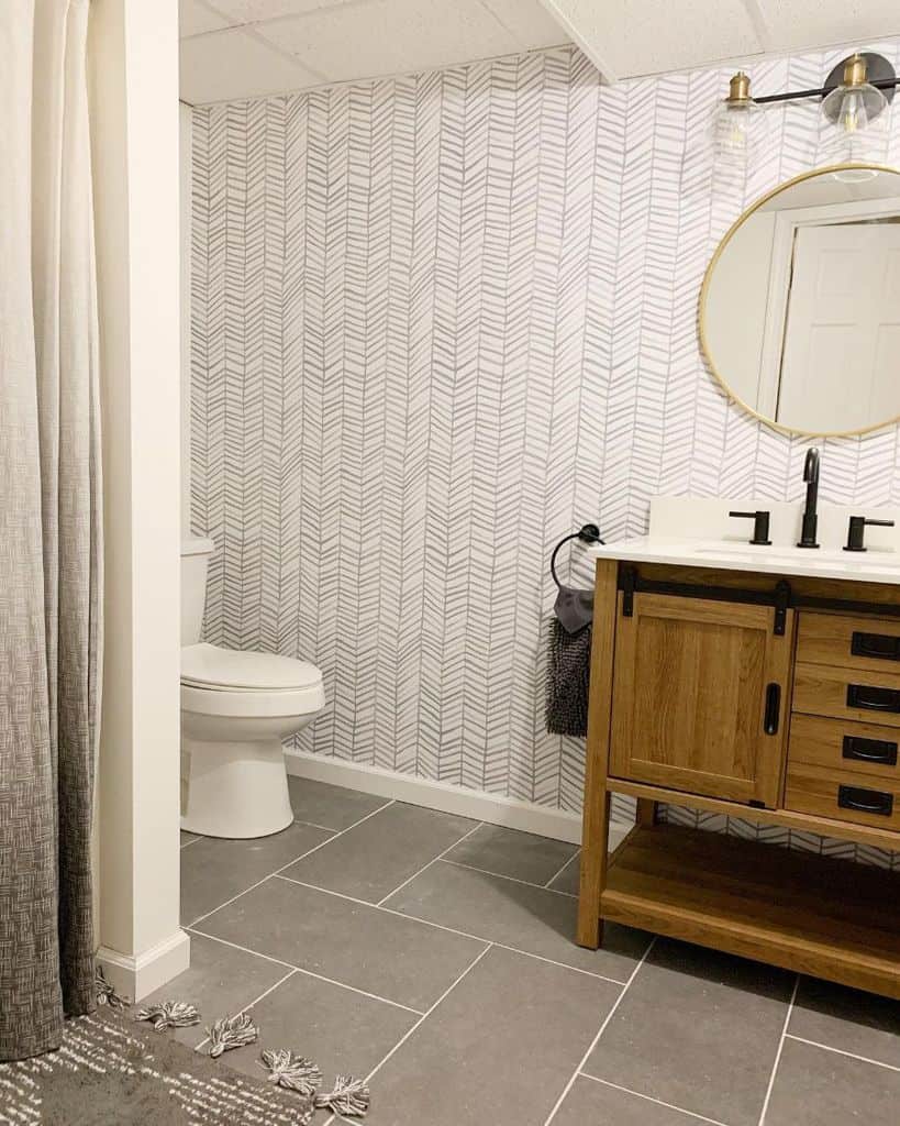 Minimalist basement bathroom with patterned wallpaper, wood vanity, and round mirror.