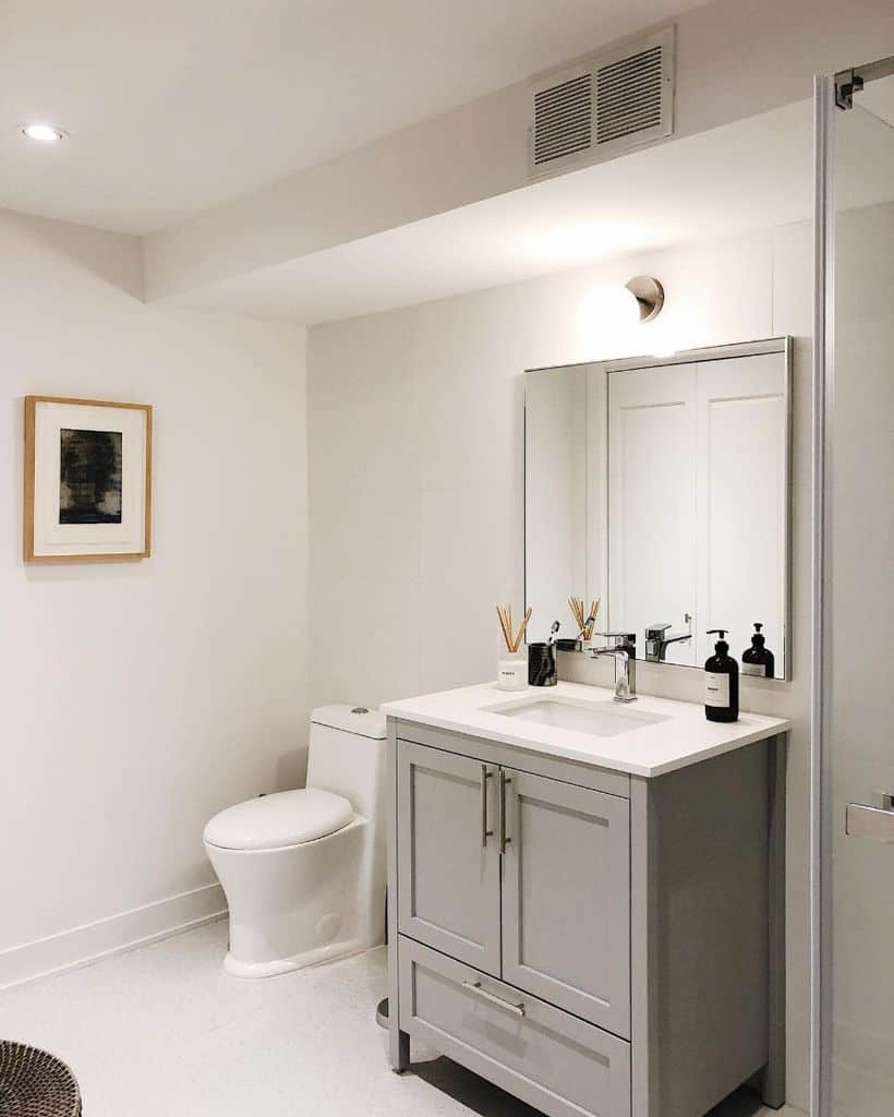 Simple white bathroom with grey vanity, framed wall art, and modern fixtures.