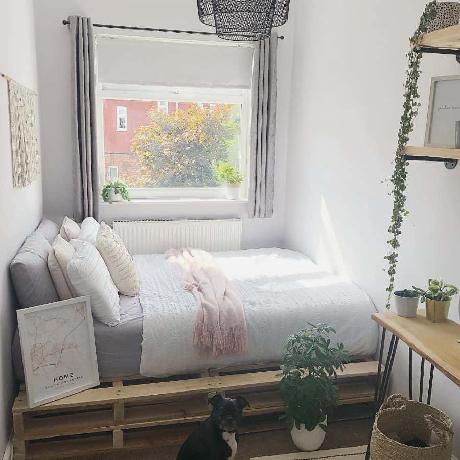 Minimalist boho bedroom with a pallet bed frame, soft neutral bedding, natural wood accents, and hanging greenery.