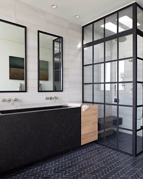 Sleek bathroom with black and wood vanity, herringbone floor tiles, and glass shower partition.