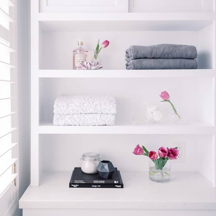 Minimalist white bathroom shelf with folded towels, flowers, and decorative accents.