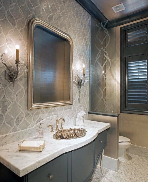 Elegant bathroom with metallic-framed mirror, marble vanity, and vintage wall sconces.