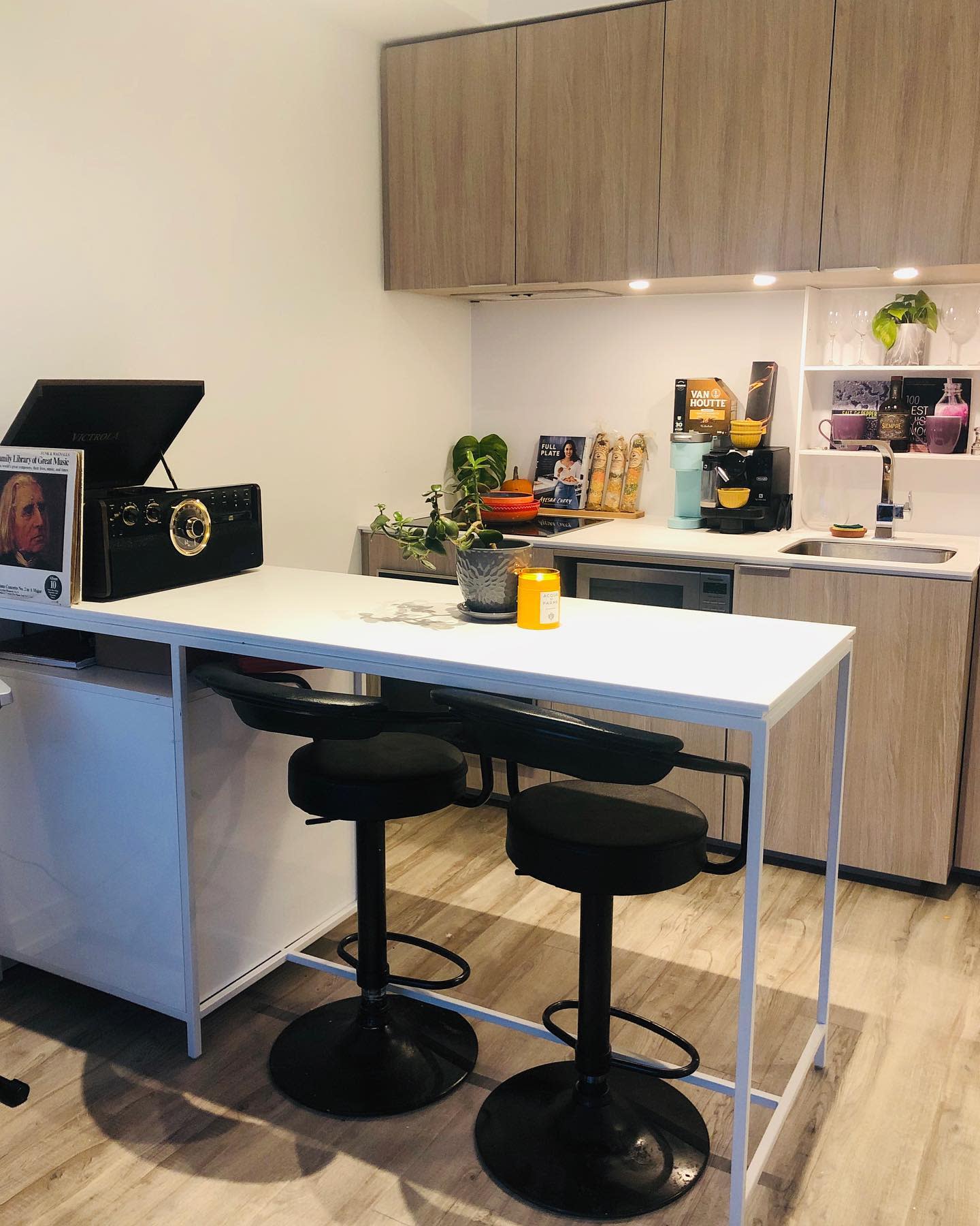 Modern kitchen with light wood cabinets, small island, and black bar stools.