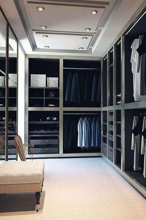 Spacious walk-in closet with neatly arranged clothes, drawers, and a cushioned bench on a light carpeted floor