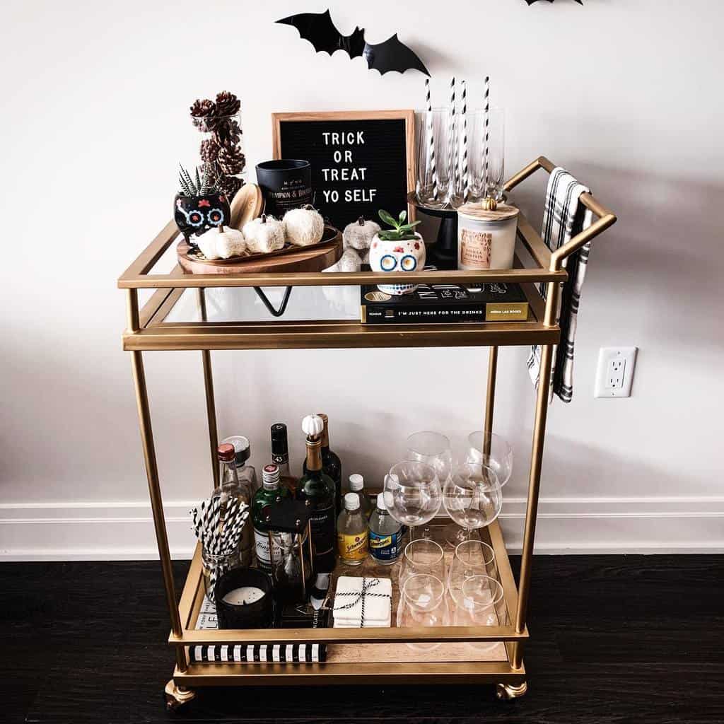 Modern gold bar cart with Halloween decorations, liquor bottles, glassware, and a "Trick or Treat Yo Self" sign.