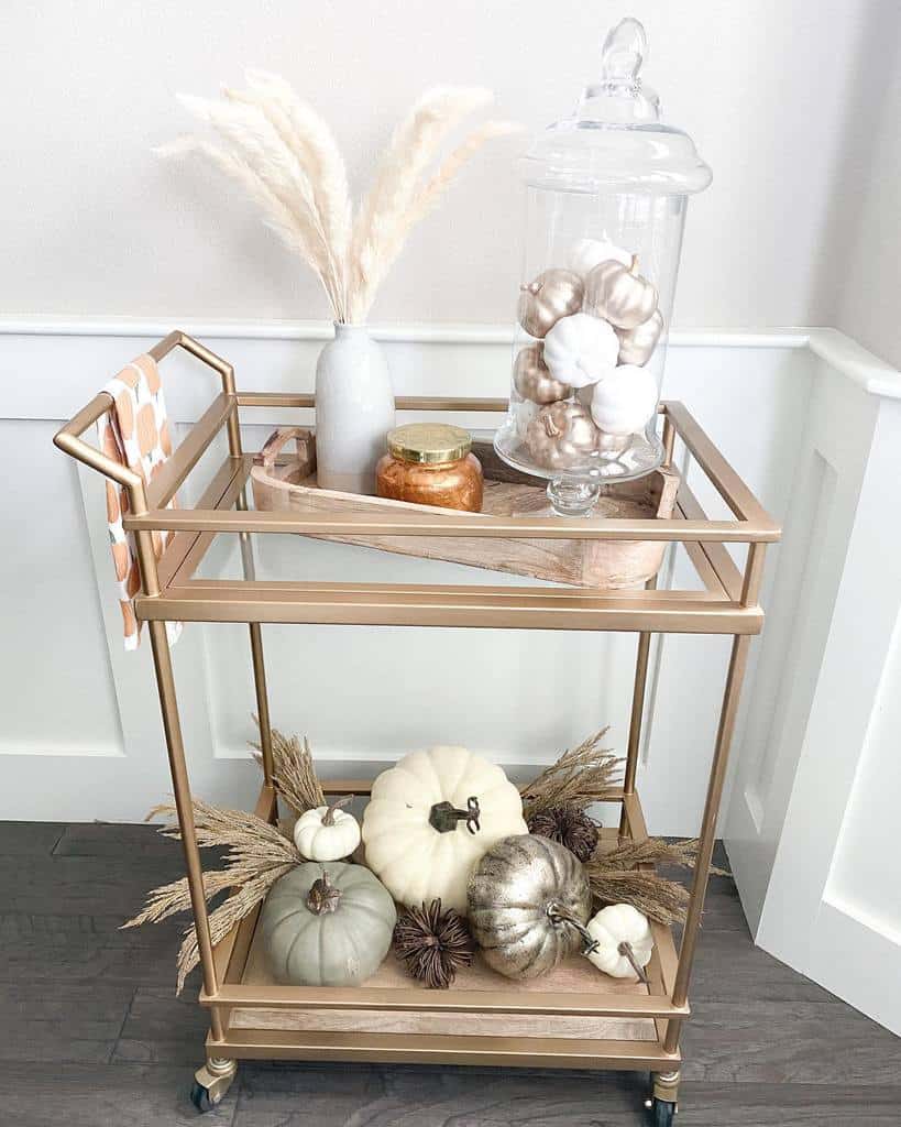 Gold bar cart with white and metallic pumpkins, pampas grass, and glass jar decor.