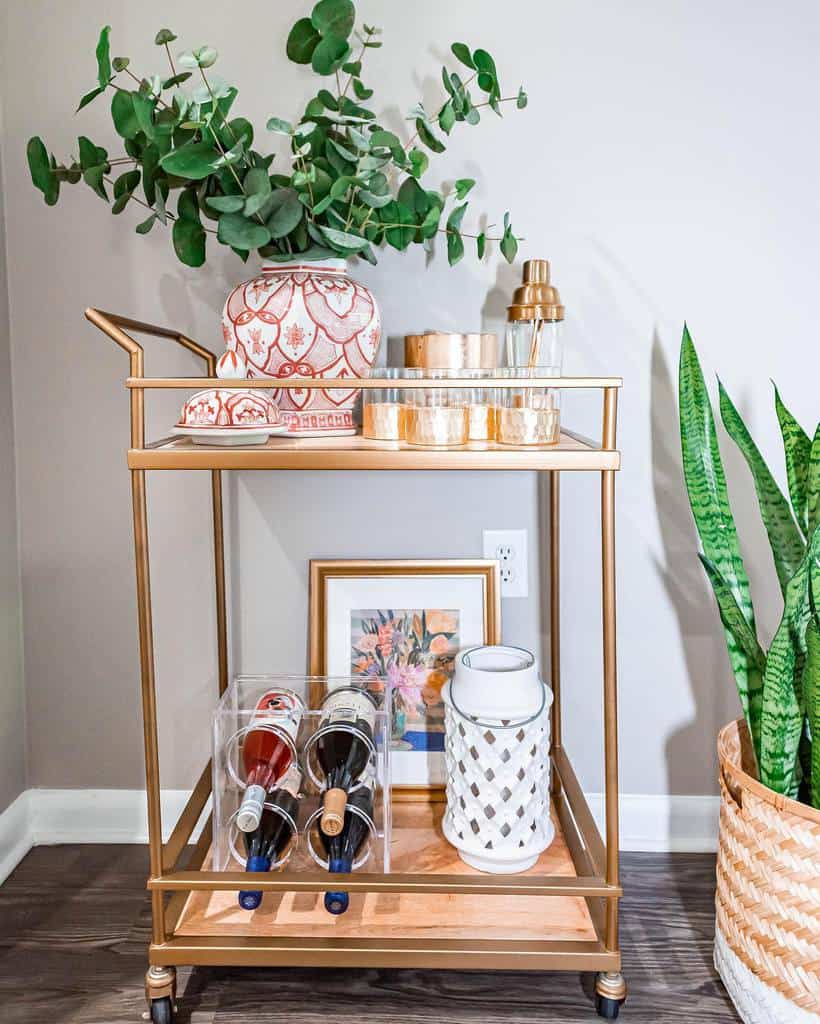 Gold bar cart with greenery, decorative jars, wine bottles, and cocktail shaker set.