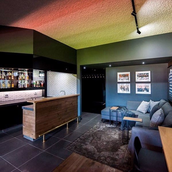 Modern man cave with a sleek wet bar, cozy sectional seating, and framed wall art.