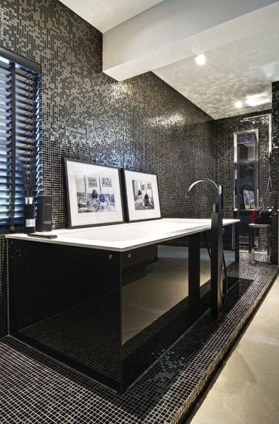 Luxurious bathroom with black mosaic tiles, elevated black bathtub, and modern decor.