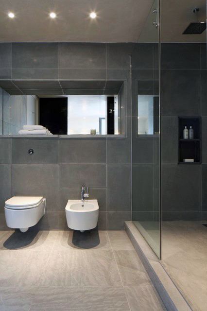 Minimalistic modern bathroom with dark gray tiles, glass shower, and wall-mounted fixtures.