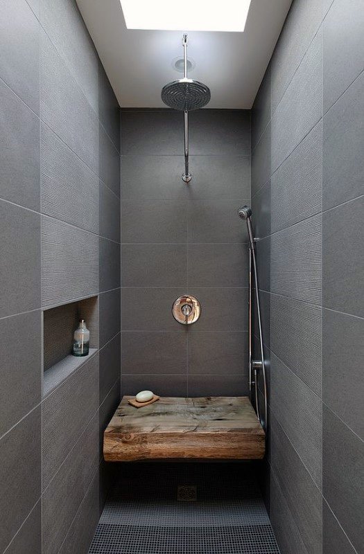 Shower with large gray tiles, built-in niche, and rustic wood bench under skylight.